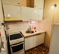 Kitchen in a 2-room apartment, white cabinets, stove, sink, floor with wood decor.
