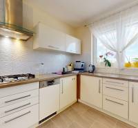 A kitchen in a family house with white cabinets, a refrigerator, and a large window.