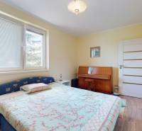 A bedroom in a family house with a bed, a piano, and a wooden decor floor.