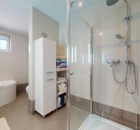 A bathroom in a family house with a bathtub, shower corner, and storage shelves.