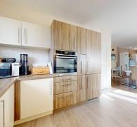 A kitchen in a family house with a wooden decor floor and a dining area in the background.