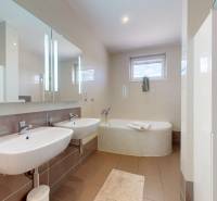 A bathroom in a family house with a double sink, a bathtub, and ceramic tiles.