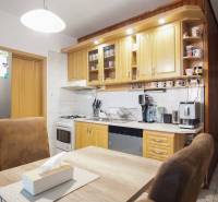 A kitchen in a 3-room apartment with a light kitchen unit, appliances, and a table with chairs.
