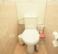 A toilet with beige tiles in a 3-room apartment with storage space for toilet paper.
