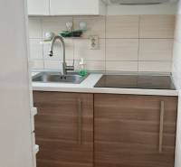A kitchen with white cabinets and a stainless steel sink in a 2-room apartment.