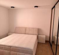 Bright bedroom of a two-room apartment with wood-patterned flooring and a comfortable bed.