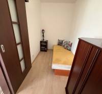 A room in a 3-room apartment with a bed, wooden decor flooring, dark furniture.