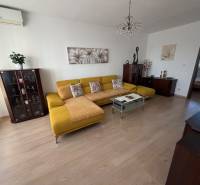 Living room with wood-patterned flooring, a yellow sofa, and a glass coffee table in a three-room apartment.