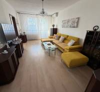 Living room with wood-patterned flooring in a three-room apartment with a yellow sofa.