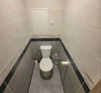 A toilet in a 2-room apartment with ceramic tile walls and flooring.