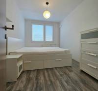 Bedroom in a 2-room apartment with a bed, light furniture, and a floor with a wooden decor.