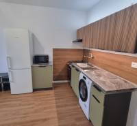 A kitchen unit in a studio apartment with a wood-patterned floor and appliances.