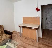 Studio apartment with a sofa, glass table, and wood-patterned flooring.