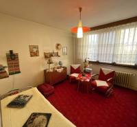 A room in a 3-room apartment with older furniture, a red carpet, and decorations.