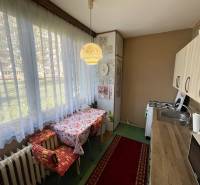 A kitchen in a 3-room apartment with a wooden decor floor and a large window with curtains.