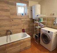 Bathroom in a family house with a bathtub, washing machine, and floor with wooden decor.