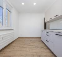 A kitchen in a 3-room apartment with a wooden decor floor and white cabinets.