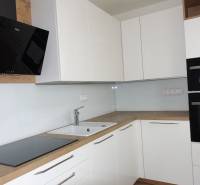 A kitchen with white cabinets and appliances, complemented by a wood-patterned floor in a three-room apartment.