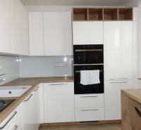 Modern kitchen with white cabinets and wood-patterned flooring in a three-room apartment.