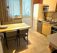 A kitchen in a 3-room apartment with a dining table, light cabinets, and a refrigerator.