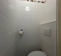 Bathroom in a studio apartment with white tiles and a wall with a decorative strip.