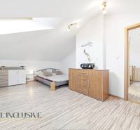 A bright bedroom with wood-patterned flooring, a dresser, and a bed in a family house.