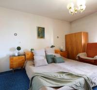 A bedroom with a large bed, wooden cabinets, and a chair in a family house.