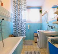 A bathroom in a family house with blue tiles, a bathtub, a washing machine, and a patterned curtain.