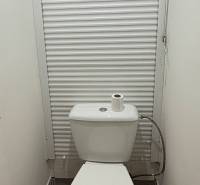 A toilet in a 2-room apartment with a white blind and tiles.