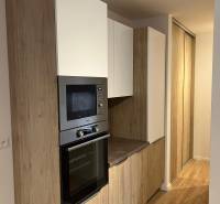 Kitchen area of a two-room apartment with a wooden decor floor and built-in cabinets.