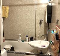 A bathroom in a 2-room apartment with a bathtub, sink, and tiled walls.