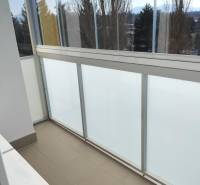 A glazed balcony in a 2-room apartment with a view of trees and mountains.