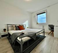 A bedroom in a two-room apartment with a wood-patterned floor and a metal bed.