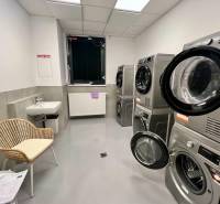 Laundry room with washing machines, dryers, a sink, and a chair in a 2-room apartment.
