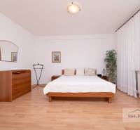Bedroom with a bed, dresser, and wooden decor flooring in a three-room apartment.