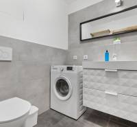 Bathroom with a washing machine and a sink, tiles, cabinet with drawers, mirror in a studio apartment.