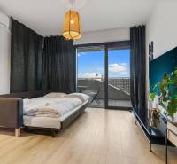 Living area in a studio apartment with a bed, wood-patterned flooring, and a balcony.