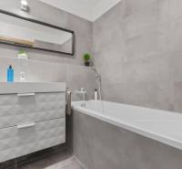 A bathroom with a bathtub, sink, and mirror in a studio apartment.