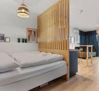 A bright room with a bed, a wooden panel, a floor with a wooden decor, and a balcony.