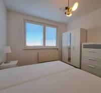 Bedroom in a two-room apartment with white furniture and a bed, window with blinds.