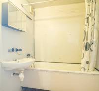 A bathroom with a bathtub and a shower curtain in a 2-room apartment, light walls, orange floor.