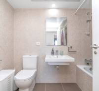 Bathroom in a 2-room apartment with a toilet, sink, bathtub, and beige tiles.