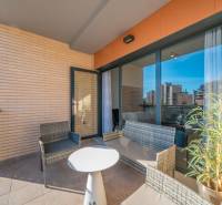 Terrace of a 2-bedroom apartment in Alicante with rattan seating and a view of the city.