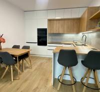 A kitchen in a 2-room apartment with a wooden decor floor, a dining table, and a bar counter.