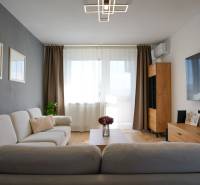 Living room in a three-room apartment with a wood-patterned floor and a large television.