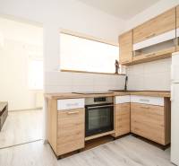 A kitchen in a 2-room apartment with a wood-patterned floor and light-colored furniture.