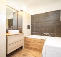 A bathroom with light tiles, a washing machine, and a floor with a wood decor in a 2-room apartment.