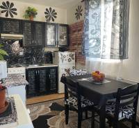 A kitchen with tables, black cabinets, and patterned curtains in a studio apartment.