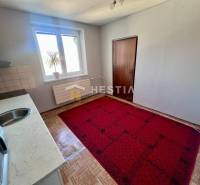 The kitchen of a three-room apartment with carpet, wooden decor flooring, and simple furnishings.