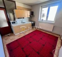 A kitchen in a 3-room apartment with a wooden decor floor and a red carpet.